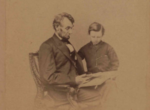 Original portrait photograph of Lincoln seated with a book and his son Tad, taken February 9, 1864